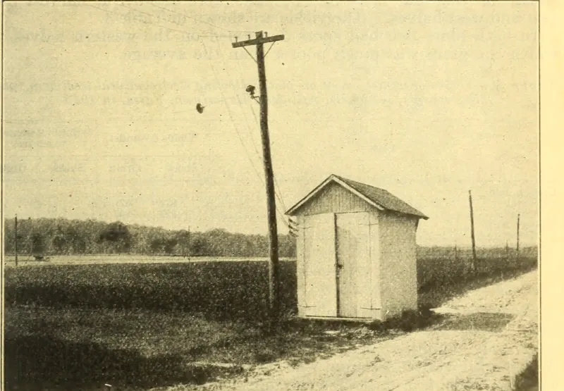 Photograph from the 1926 USDA bulletin: a wooden pole with insulators beside a small white apparatus house at the edge of the Arlington test field